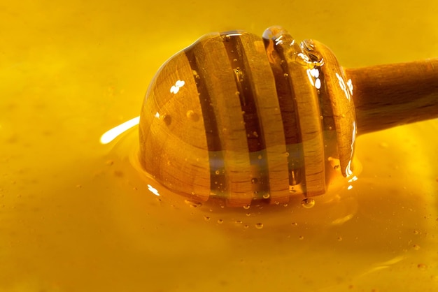 Miele che gocciola dal mestolo di miele nella ciotola di legno Primo piano Organico sano