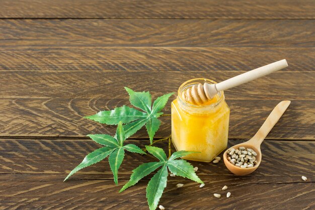 Miele di cannabis in una ciotola con legno più profondo, foglie di canapa e semi sul tavolo di legno.