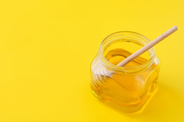 Miele di fiori liquidi in vaso di vetro con cucchiaio di miele in legno.