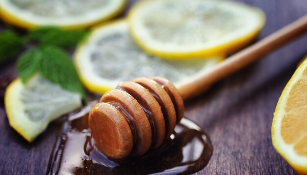 Miele e limone. Bastone di miele e fette di limone a fette sul tavolo di legno. Tè in tazza e miele di tiglio dolce in barattolo.