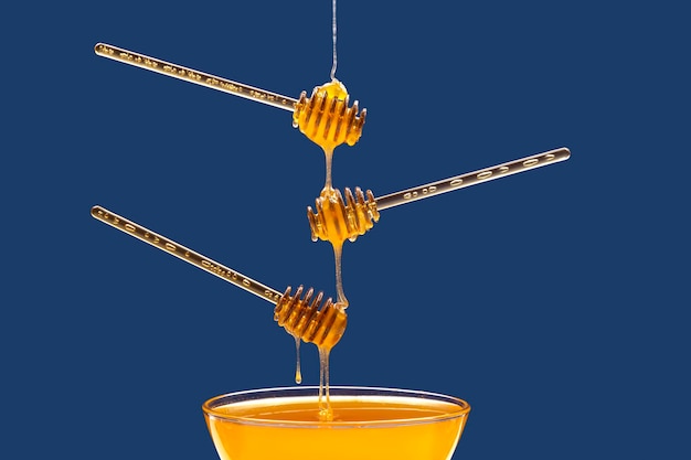 Miele floreale fresco gocciola da un cucchiaio in un cucchiaio su uno sfondo blu. Cibo vitaminico biologico.