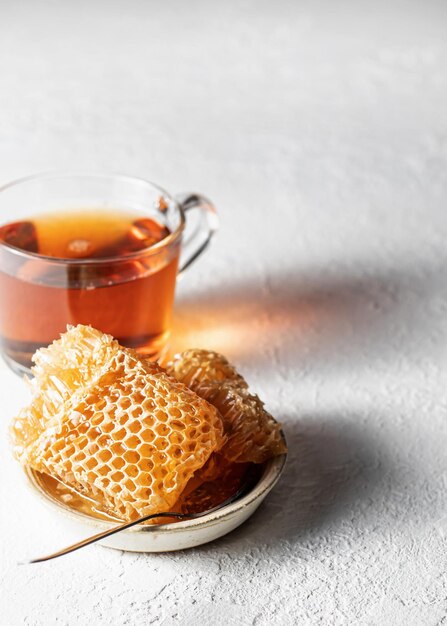 Miele in nido d'ape in un piattino con cucchiaio e tazza di tè su sfondo bianco Posto di testo