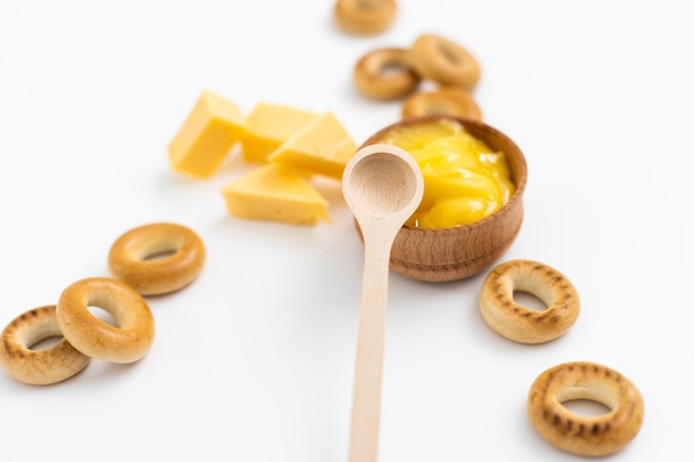 miele in una ciotola di legno, bagel e formaggio su sfondo bianco.