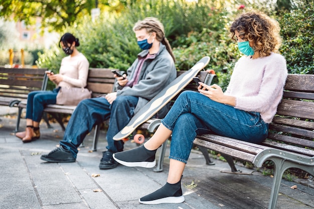 Milenial persone che guardano video su smartphone con maschera facciale sulla terza ondata di Covid