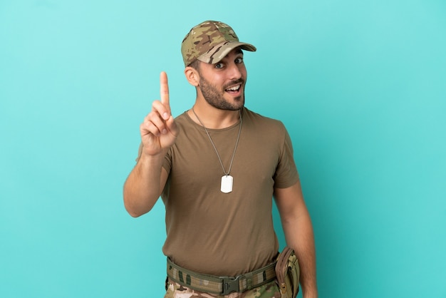 Militare con dog tag sopra isolato su sfondo blu che mostra e solleva un dito