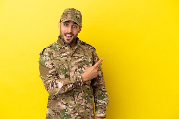 Militare isolato su sfondo giallo che punta al lato per presentare un prodotto