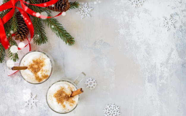 Milkshake natalizio a base di eggnog fatto in casa con cannella servito in due tazze su uno sfondo di pietra o ardesia