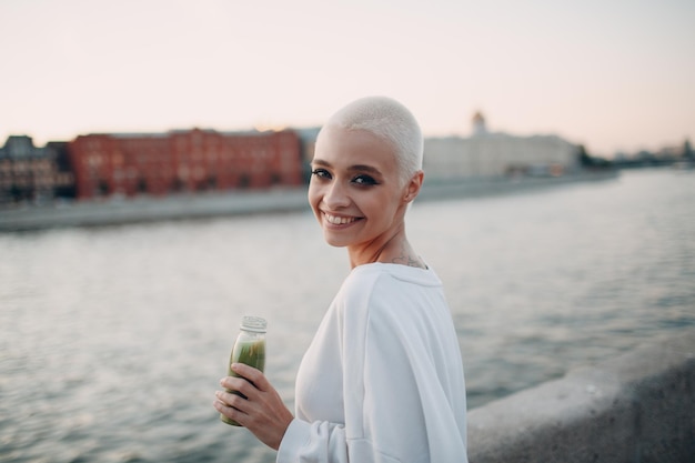 Millenial giovane donna bionda capelli corti all'aperto con frullato verde