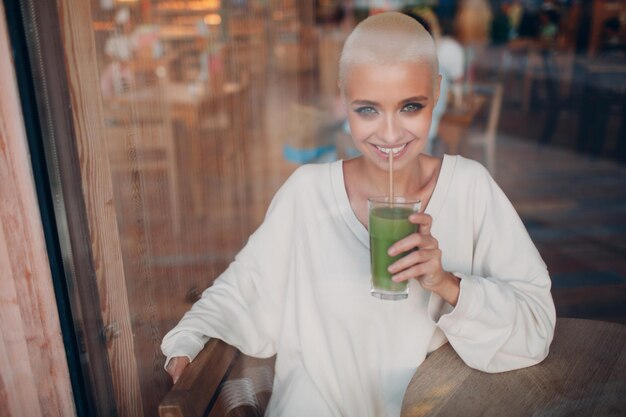 Millenial giovane donna bionda capelli corti indoor con frullato verde