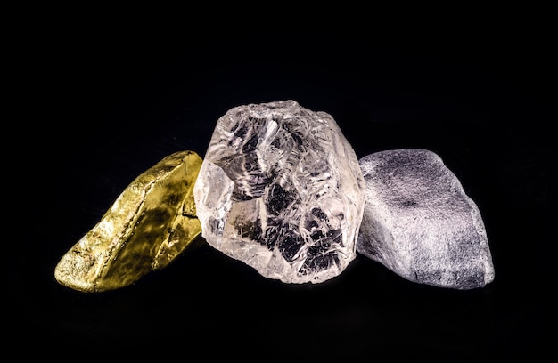 Minerale d'argento, pepita d'oro e diamante grezzo su superficie nera isolata.