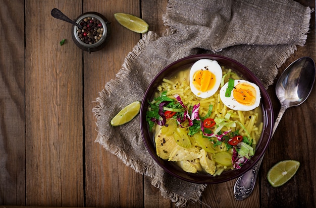 Minestra di pasta con pollo, sedano e uovo in una ciotola su un vecchio tavolo di legno.