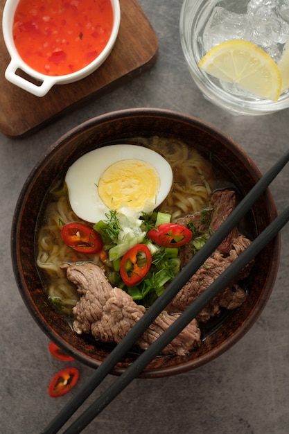 Minestra di ramen asiatica con manzo, uovo, erba cipollina in ciotola su gray.