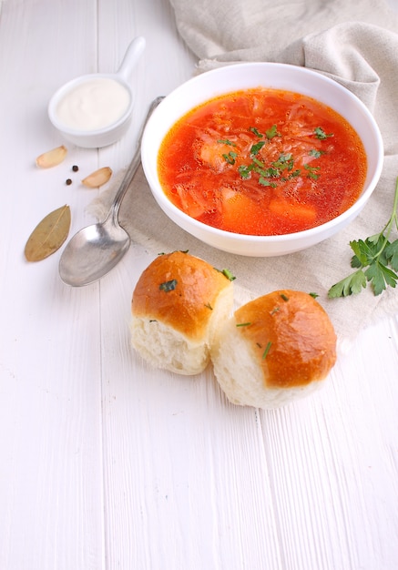 Minestra rossa del borscht in ciotola bianca con panna acida e prezzemolo, vista superiore, su fondo bianco di legno.