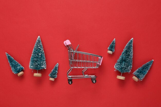 Mini alberi di Natale e carrello della spesa su sfondo rosso Capodanno o Natale sfondo