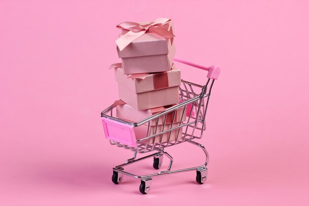 Mini carrello del supermercato con scatole regalo su pastello rosa