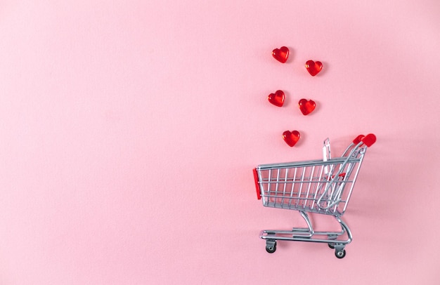 Mini carrello e cuori di vetro su sfondo rosa