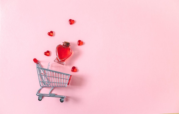 Mini carrello una bottiglia di profumo di cuore e cuori decorati in vetro su sfondo rosa