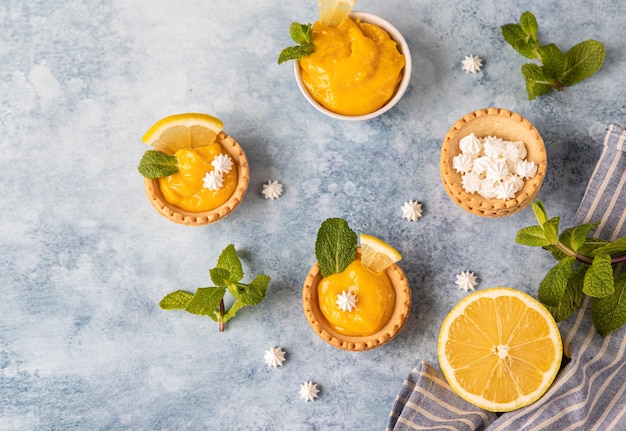 Mini crostate con lemon curd, mini meringa, fette di limone e menta su fondo blu in cemento