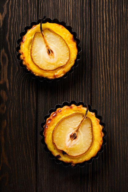 Mini crostate delle pere e della crema su un vecchio fondo di legno della tavola di marrone scuro