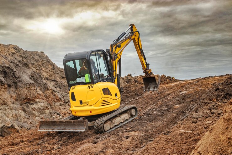 Mini escavatore in cantiere sul bordo di una fossa contro un cielo blu nuvoloso Attrezzatura da costruzione compatta per lavori di sterro Un assistente indispensabile per i lavori di sterro