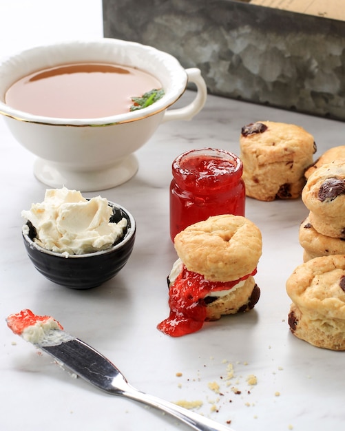 Mini focaccine rotonde con marmellata di fragole e panna rappresa e una tazza di tè, fondo in marmo bianco