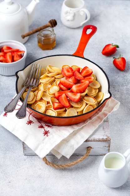 Mini frittella di cereali bianco con fragole in padella per colazione sulla superficie grigia. Vista dall'alto.