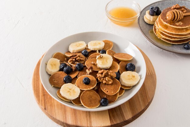 Mini frittelle alimentari di tendenza con frutti di bosco e fette di banana in una ciotola su una tavola rotonda di legno deliziosa colazione