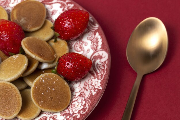 Mini pancake di cereali fatti in casa con yogurt, miele e fragole sul tavolo colorato.