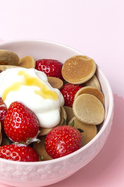 Mini pancake di cereali fatti in casa con yogurt, miele e fragole sul tavolo colorato.