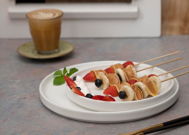 Mini pancake dolci, serviti con crema spalmabile al burro di arachidi, fragole e mirtilli rossi in uno spiedino.Primo piano