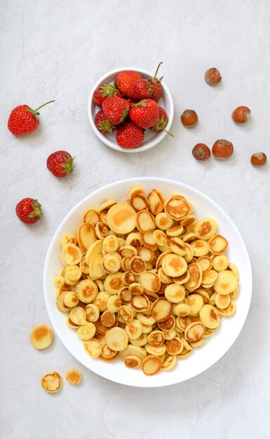 Mini pancake in una ciotola con fragole fresche su uno sfondo chiaro