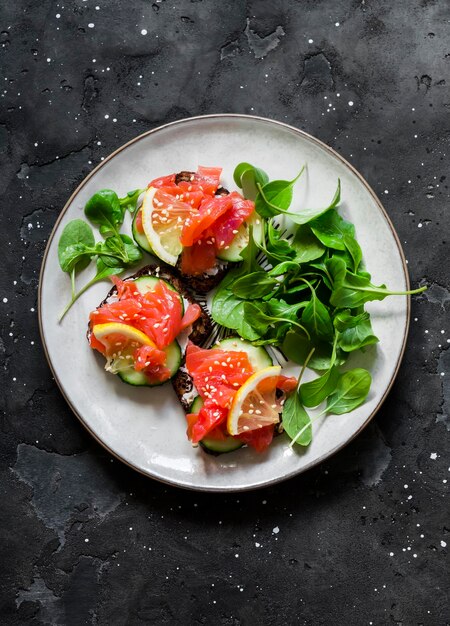 Mini panini con pane di segale crema di formaggio salmone e cetriolo su sfondo scuro vista dall'alto Delizioso antipasto di tapas per la colazione