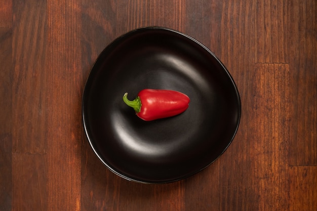 Mini peperone rosso che risiede in un bawl nero isolato su fondo di legno. Vista dall'alto