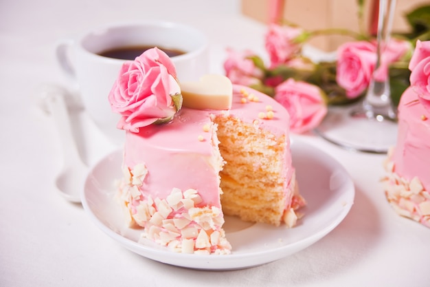 Mini piccola torta con glassa rosa, bellissime rose, tazza di caffè, confezione regalo sul tavolo bianco.