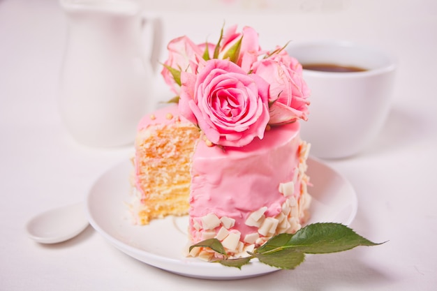 Mini piccola torta con glassa rosa, bellissime rose, tazza di caffè sul tavolo bianco.