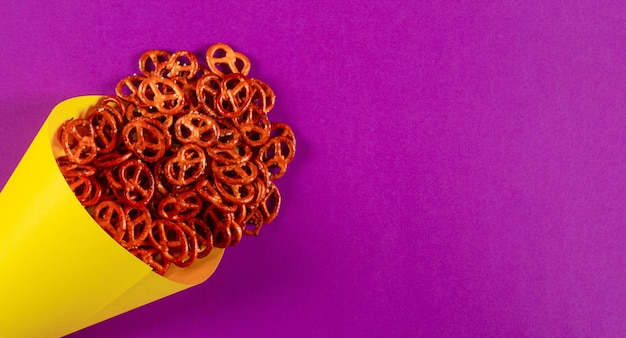 Mini pretzel in cono di carta gialla giacciono su sfondo viola con spazio vuoto per il testo