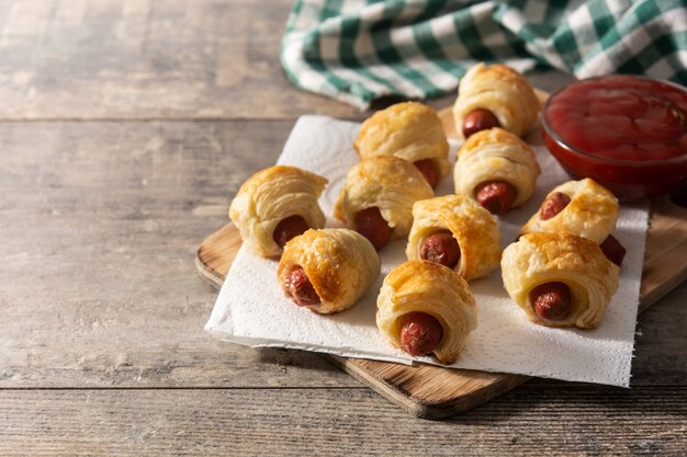 Mini salsicce avvolte in pasta sfoglia con salsa ketchup sul tavolo di legno