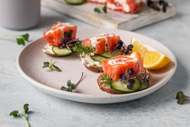 Mini sandwich aperti con salmone, crema di formaggio, cetriolo e microgreen su pane di segale.