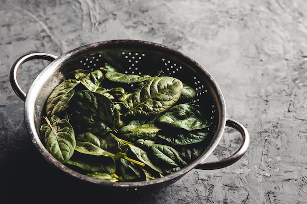 Mini spinaci freschi in uno scolapasta sul vecchio tavolo di cemento. Cibo sano, prodotto ecologico. Vegano