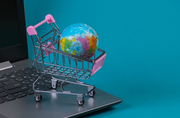 Mini supermarket trolley with globe on laptop keyboard. Blue  background. Online shopping