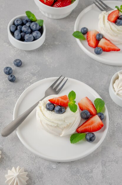 Mini torta meringata Pavlova con panna montata e frutti di bosco freschi in cima su un piatto.