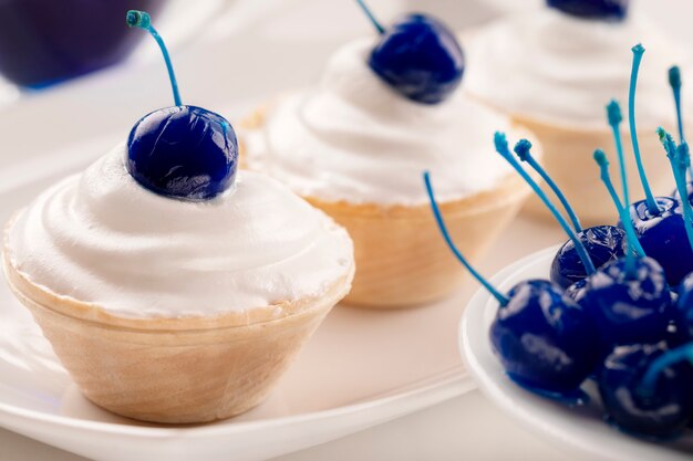 Mini torte con crema di formaggio decorato bacche di ciliegia in scatola blu. Avvicinamento