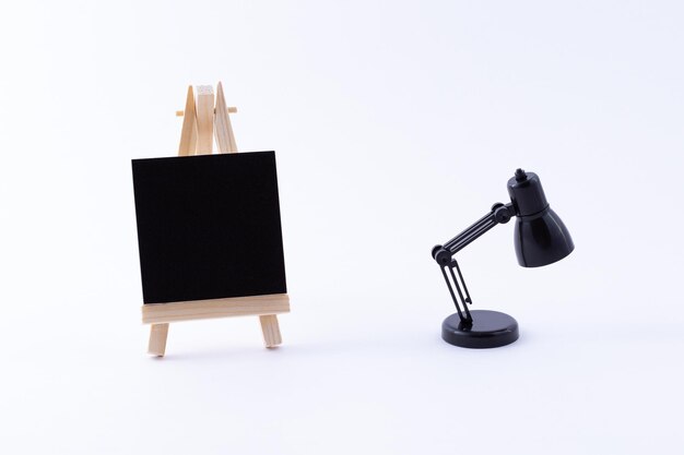 Miniatura da cavalletto in legno con tela quadrata nera vuota e lampada da tavolo