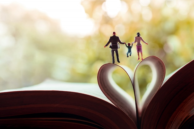 Miniatura di padre, madre e figlio che si tengono per mano e che camminano verso il libro su una pagina come a forma di cuore