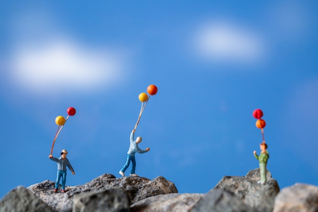 Miniatura persone, felice famiglia azienda palloncino sulla roccia con cielo blu