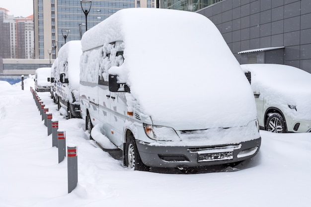 Minibus bianchi hanno nevicato durante una tempesta di neve in inverno nel parcheggio.