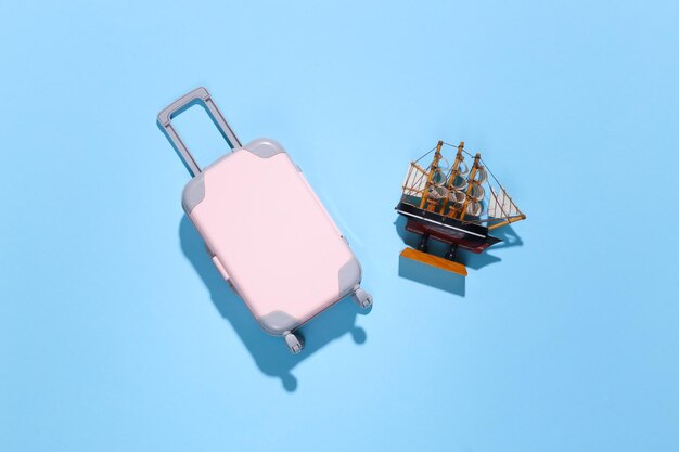 Minimalismo da viaggio. Mini valigia da viaggio in plastica e nave su sfondo blu con ombra profonda. Stile minimale. Vista dall'alto, posizione piatta