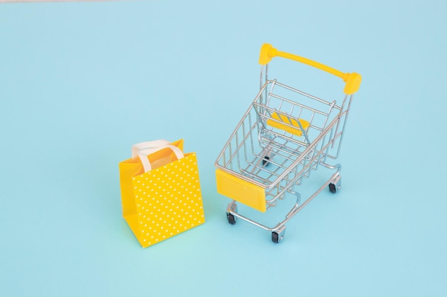 Minimalismo del concetto di consumatore Mini carrello della spesa per lo shopping su sfondo colorato vista dall'alto