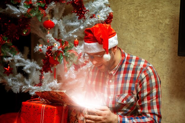 Miracolo di Natale. Nerd apre il suo regalo con il cappello di Babbo Natale. Atmosfera natalizia, Capodanno.