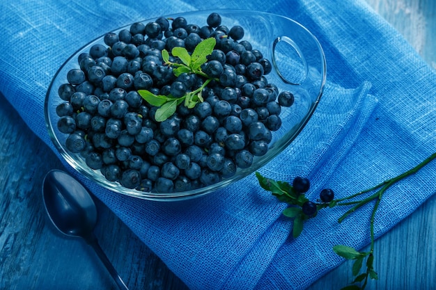 Mirtilli freschi in ciotola di vetro. Mirtilli succosi e freschi con foglie verdi sul tavolo di legno blu. Concetto per una sana alimentazione e nutrizione.